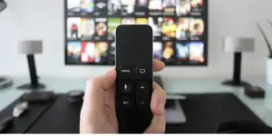 a man's hand holding a remote in front of a TV set