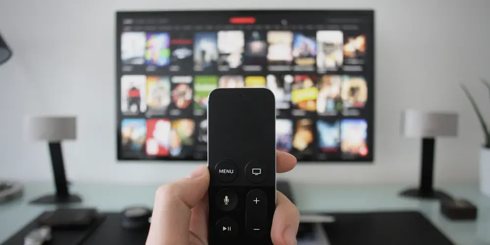 a man's hand holding a remote control in front of the TV